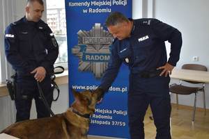 dwaj policjanci i pies, jeden z nich dotyka policyjnego psa