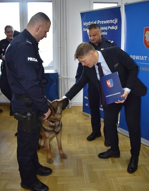 dwaj policjanci w mundurach, policyjny pies, nad którym nachyla się starosta