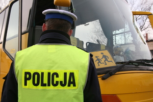 policjant stojący tyłem w białej czapce w tle żółty autokar do przewozu dzieci
