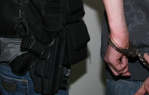 ręce w kajdankach i broń policyjna przy pasie funkcjonariusza