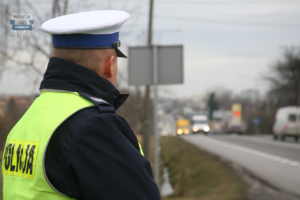 policjant z drogówki w żółtej kamizelce stoi na poboczu drogi