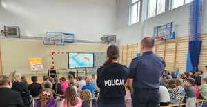 policjantka i policjant oraz grupa dzieci na sali oglądają na ekranie film profilaktyczny