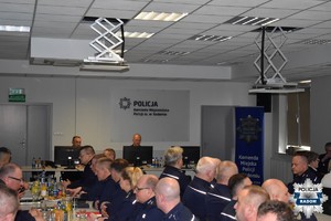 zdjęcie z odprawy, grupa umundurowanych policjantów siedzi przy stołach