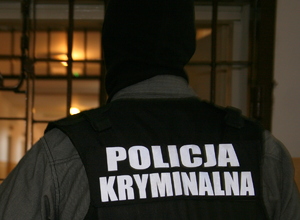 mężczyzna stoi tyłem w kominiarce w czarnej kamizelce z napisem Policja Kryminalna