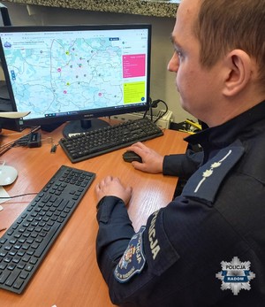 policjant siedzi przy biurku patrzy w monitor, na biurku 2 klawiatury