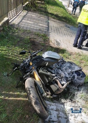 rozbity motocykl lezy na poboczu, w tle policjant