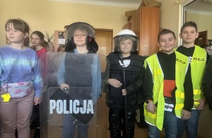 dzieci w pomieszczeniu służbowym przymierzaja policyjne wyposazenie