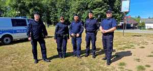 czterech policjantów i policjanta stoją na trawie w tle radiowóz