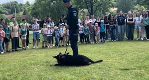 policjant z psem policyjnym prowadzący prelekcje na temat pracy z czworonogiem, w tle dzieci