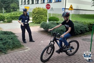 chłopiec jedzie na rowerze obok stoi policjantka