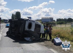 pojazd lezy na boku na jezdni, obok policjant i uczestnicy wypadku