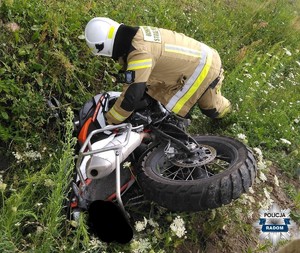 motocykl lezy w rowie obok strażak próbuje go podnieść