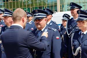 mężczyzna przypina medal policjantowi, w tle grupa policjantów