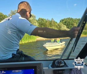 policjant siedzi na policyjnej łodzi  w tle holowana łodź