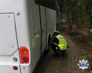 policjant nachyla sie przy białym autobusie i sprawdza stan techniczny