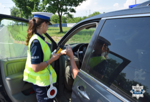 policjantka stoi przy pojeździe i kontroluje kierowcę, trzyma dokumenty policyjna tarcze i alkomat