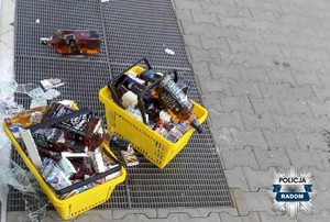 w żółtych koszykach sklepowych zapakowane skradzione produkty alkohol i papierosy, koszyki stoją na chodniku