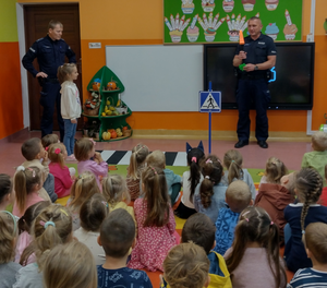 policjanci w klasie, dzieci siedzące na dywanie słuchając policjantów, twarze dzieci niewidoczne