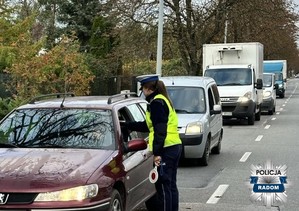 policjantka stoi przy aucie i kontroluje  trzeźwośc kierowcy, w tle kilka pojazdów czekających na kontrole