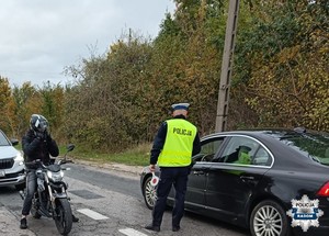 policjant jest tyłem stoi przy auie kontroluje kierowcę, po lewej stronie widac motocyklistę, który czeka na badanie trzeźwości