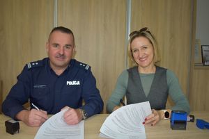 policjant i kobieta siedzą przy stole, na którym leżą kartki będa podpisywac porozumienie