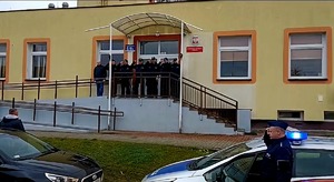 grupa policjantów na schodach przed budynkiem oddaje hołd, na pierwszym planie radiowozy