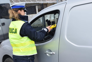 policjantka stoi przy aucie i kontroluje trzeźwość kierowcy