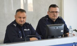 przy stoliku siedzi dwóch policjantów po prawej męzczyzna ma okulary, przed nimi monitor