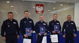 zdjęcie grupowe 5 policjantów, trzech z nich trzyma teczki z dyplomami i torby papierowe z nagrodami