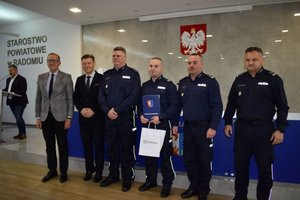 zdjęcie grupowe 4 policjantów, 2 mężczyzn, w tle męzczyzna stoi przy mikrofonie