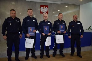 5 policjantów, w środku 3 z nich trzyma teczki i torby z nagrodami