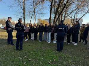 przed budynkiem grupa młodziezy i troje policjantów stojących tyłem