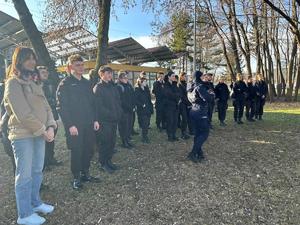 grupa uczniów i policjanta przed budynkiem komendy