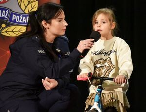 dziewczynka na rowerku obok niej kuca policjantka mi trzyma mikrofon