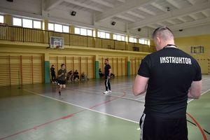 policjant na sali gimnastycznej w tle męzczyzna biegnacy obok policjant