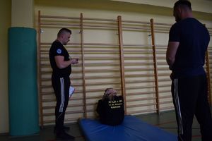 dwaj policjanci w strojach sportowych i uczennica przy drabince robiaca brzuszki