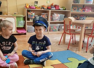 dwoje dzieci na dywanie, chłopiec ma policyjna czapkę