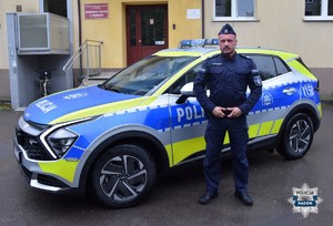przed budynkiem komisariatu policyjny radiowóz obok stoi policjant