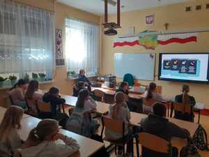 na sali lekcyjnej uczniowie siedza w ławkach w tle policjantka oglądaja film profilaktyczny