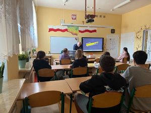 spotkanie z uczniami w klasie, dzieci siedza w ławkach widac ich tyłem w tle policjant, widac ekran