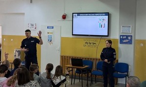 policjanci na spotkaniu w szkole w tle ekran widac głowy uczniów