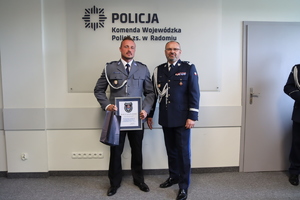 na zdjęciu dwaj policjanci w pomieszczeniu jeden z nich trzyma podziękowania w ramce