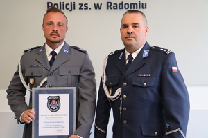 na zdjęciu dwaj policjanci w pomieszczeniu jeden z nich trzyma podziękowania w ramce