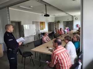 policjant rozmawia z seniorami, którzy siedzą przy stole