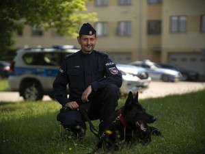 policjant i pies słuzbowy przed budynkiem komendy