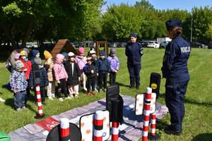 na placu przed budynkiem grupa dzieci i funkcjonariusze oraz mini miasteczko ruchu drogowego