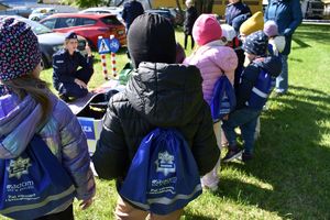 widac grupę dzieci stojących tyłem do aparatu w tle kuca policjantka