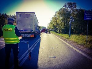 miejsce wypadku na ulicy po lewej stronie stoi tyłem do aparatu policjant w kamizelce w tle pojazd ciężarowy