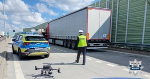 na ulicy pojazd cięzarowy i idacy w jego kierunku policjant, radiowóz, a za nim dron