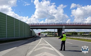policjant na srodku drogi trzyma policyjna tarcze i chce zatrzymac pojazd cięzarowy do kontroli